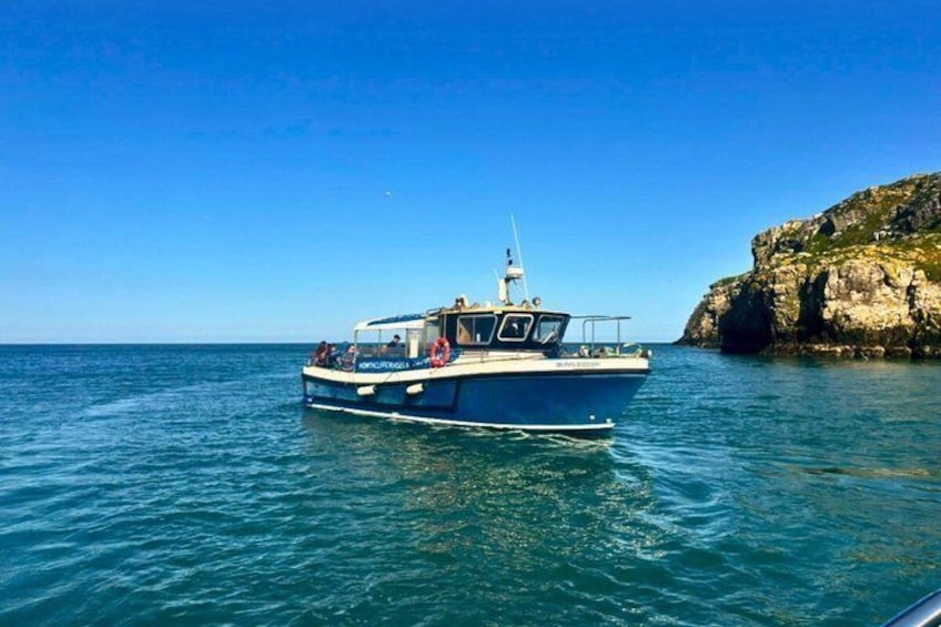 A blue boat with a cabin and a mast, anchored near a rocky coastline. 1