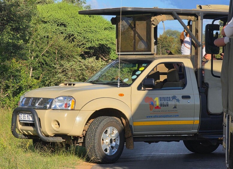 A beige safari vehicle with a roof rack and a sign reading '1 AFRICA MOJA Genuine African Adventures.' 1