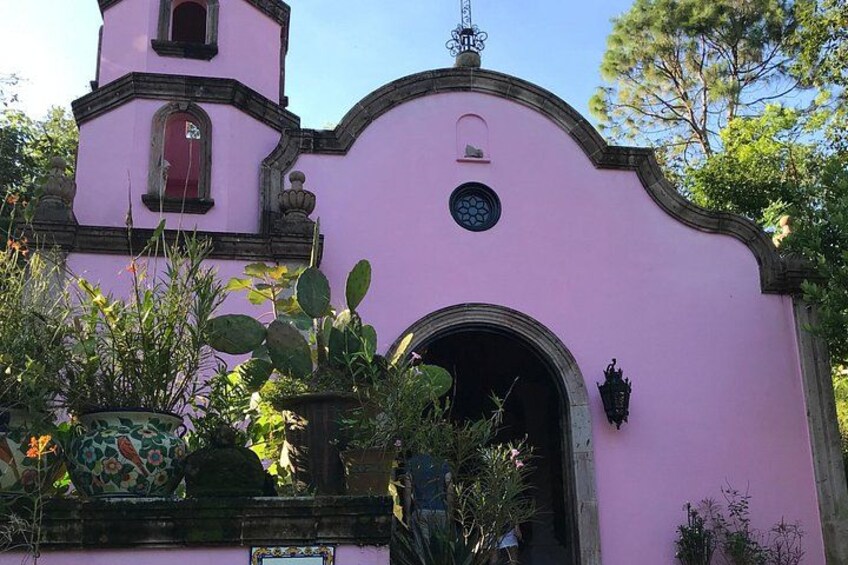 Een roze kerk met een klokkentoren, een rondboogvormige ingang en decoratieve details. 5