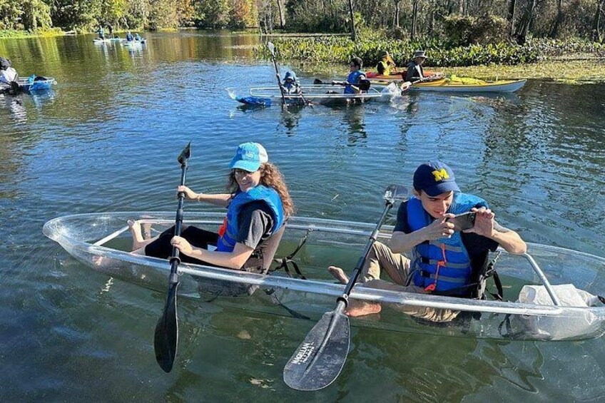 Dos personas en una canoa transparente en un lago tranquilo, remando con remos. 2