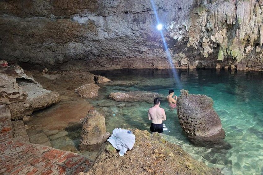 A cave with clear water, rocks, and a person taking a photo. 4