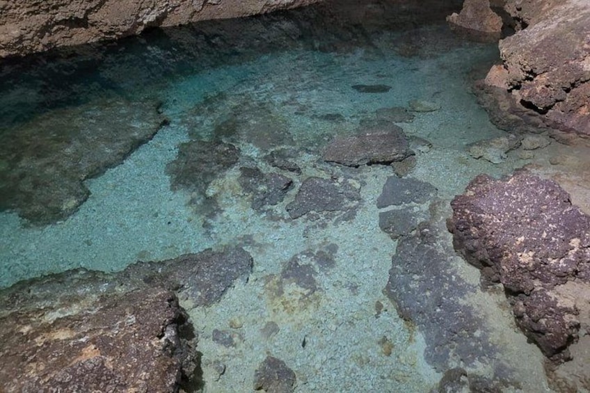 A rocky cave interior with clear water and large boulders. 2