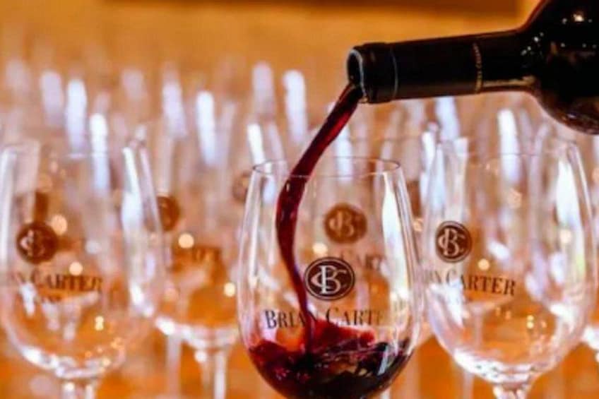 A bottle pouring red liquid into a glass with a logo. 1