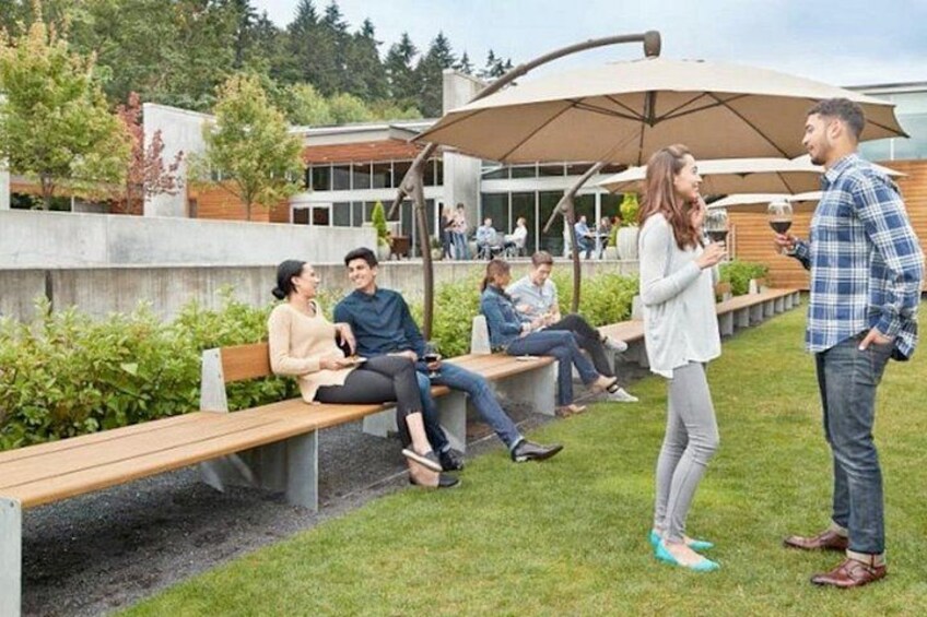 A park with benches, people sitting and standing, and a building in the background. 3