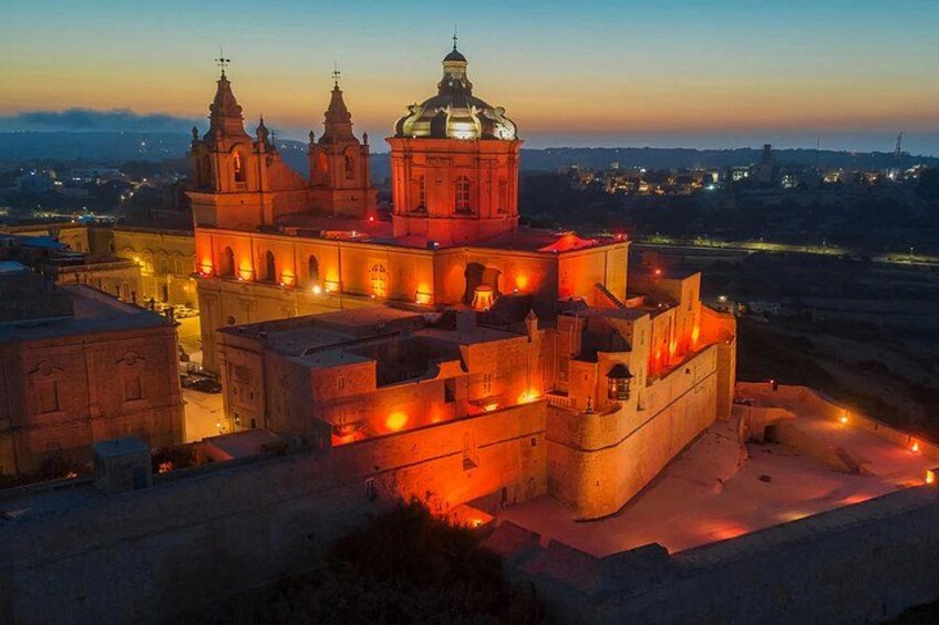 A historic fortress with multiple towers and a large dome, illuminated at dusk. 4