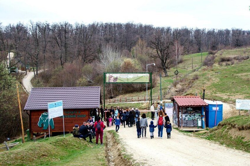 Un chemin de terre bordé d’une foule de personnes, une structure en bois portant l’inscription « JUGENDSHOP », et un bâtiment bleu avec une enseigne. 3