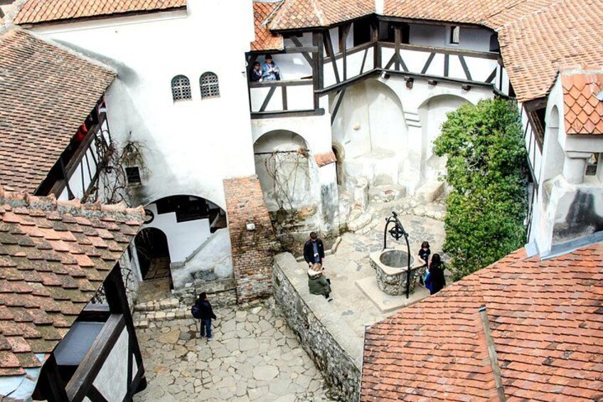Une ruelle pavée bordée de bâtiments historiques, avec un puits et des passants. 5