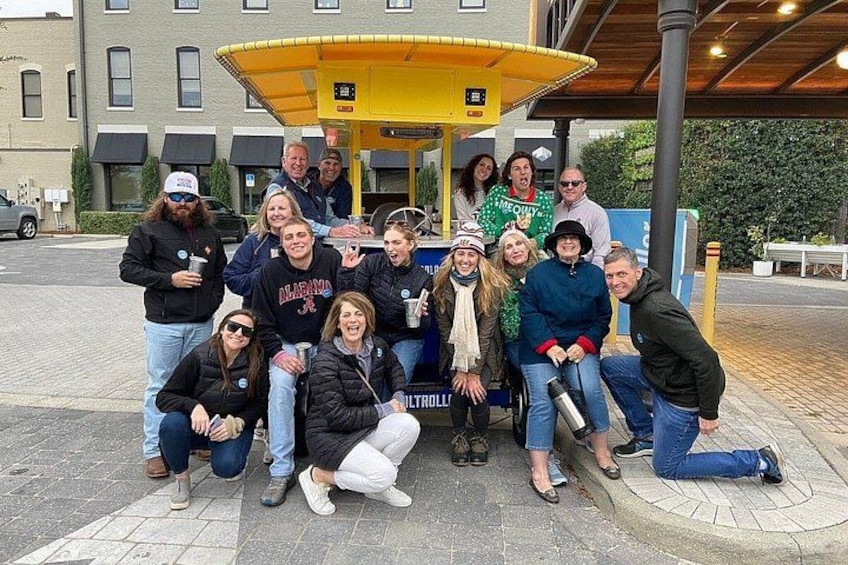 A group of people posing in front of a yellow kiosk with a sign that reads 'MERCY.' 2