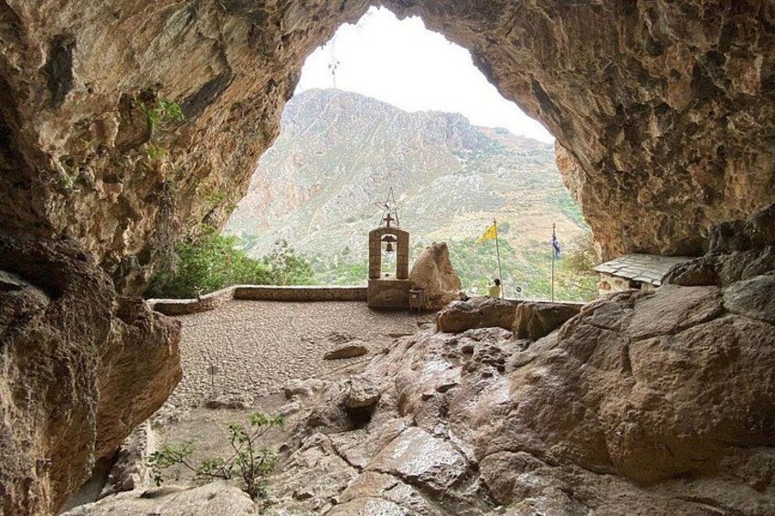 A cave entrance with a small structure inside, rocky terrain, and a mountainous landscape in the background. 5