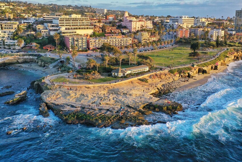 Eine Küstenstadtlandschaft mit felsiger Küste, wo Wellen auf den Strand branden, und im Hintergrund eine Mischung aus Wohn- und Geschäftsgebäuden. 5