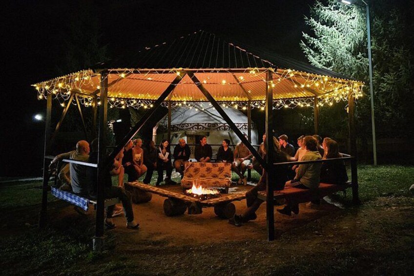 A gazebo with string lights, a fire pit, and people sitting around. 5
