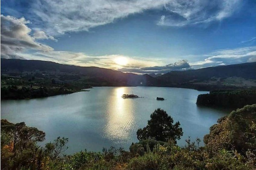 Un lac paisible avec une petite île, entouré de collines et d’arbres, sous un ciel partiellement nuageux. 4