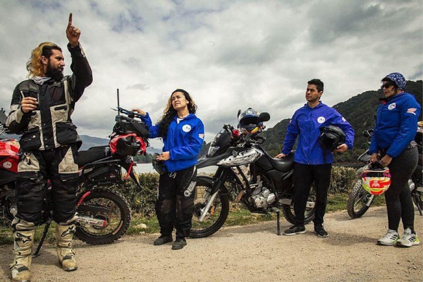 Un groupe de personnes se tient à côté de motos sur un chemin de terre, avec des montagnes en arrière-plan. 1