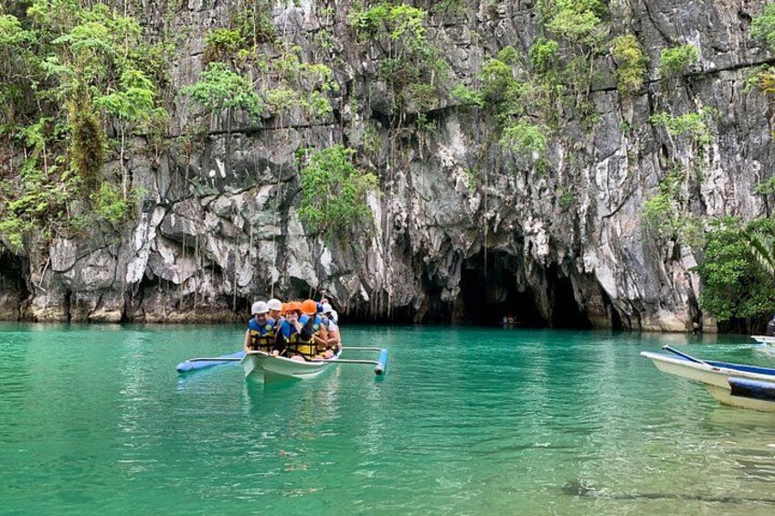 A boat with passengers navigating through a clear turquoise waterway, with a rocky cliff in the background. 1