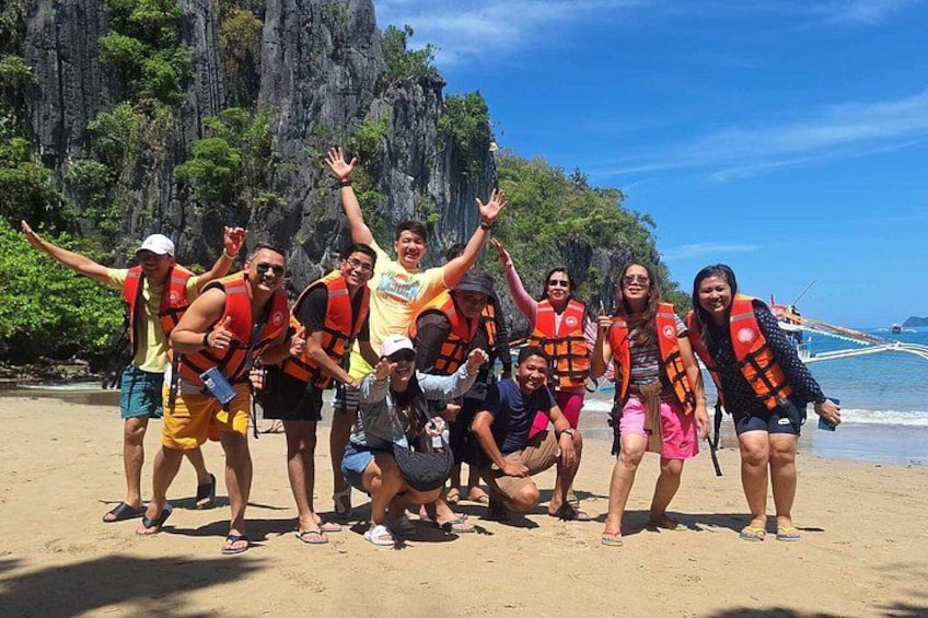 A group of people on a sandy beach with rocky cliffs in the background. 5