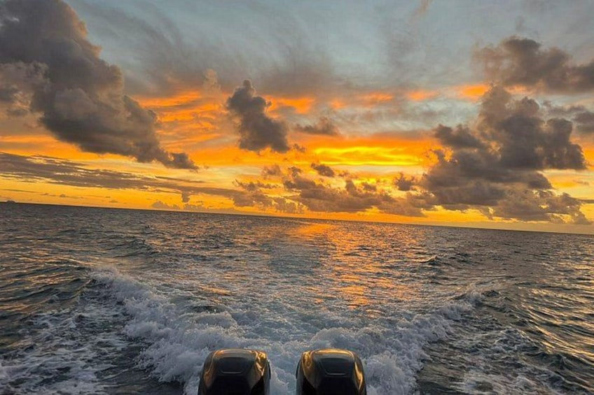Een boot vaart door woelig water, met een zonsondergang op de achtergrond. 1