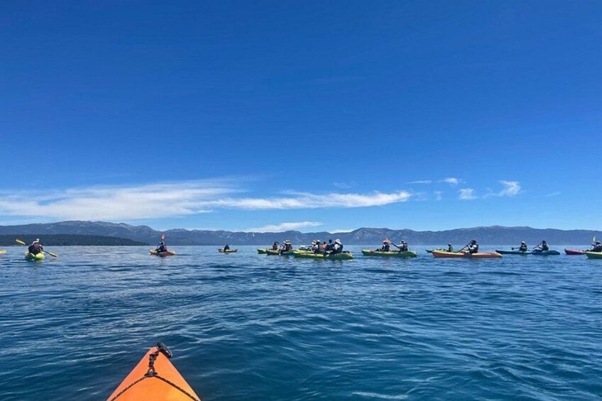 A group of kayakers on a calm body of water with mountains in the background. 2