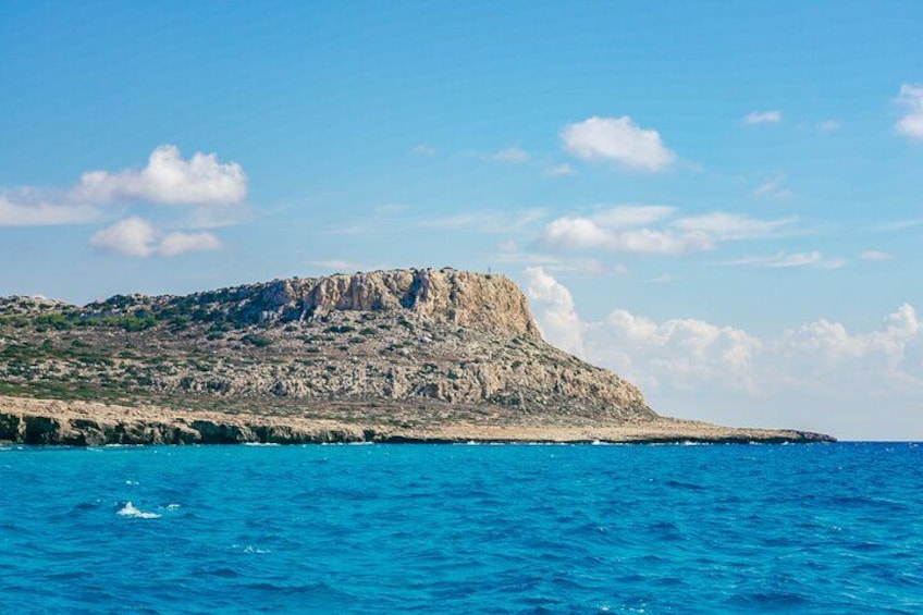Un paisaje costero con una colina rocosa y mar azul claro. 3