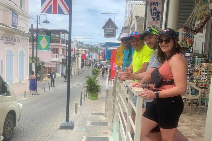 A street scene with a group of people standing by a railing, a flag, and storefronts. 3
