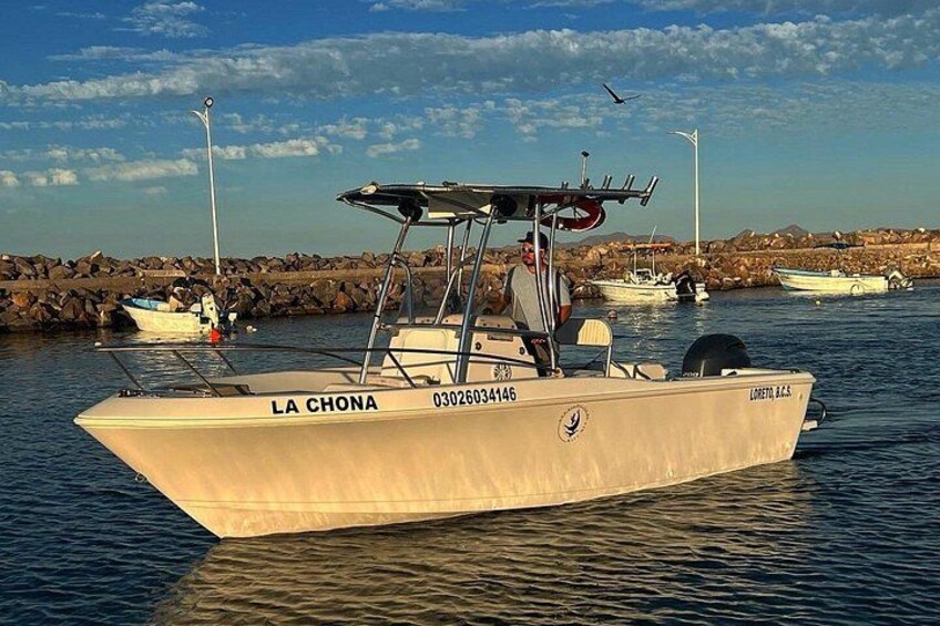 Ein Boot namens 'LA CHONA' liegt an einem felsigen Ufer, im Hintergrund sind weitere Boote zu sehen. 1