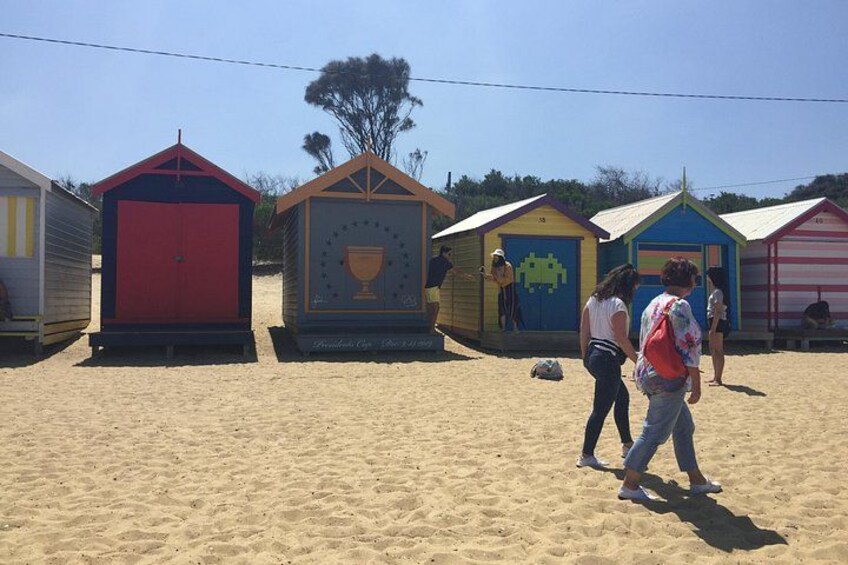 Kleurenrijk ontworpen strandhutten, een zandstrand en enkele mensen die er lopen. 3