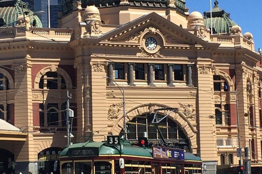 A historic building with ornate architecture, a clock, and a tram in front. 3