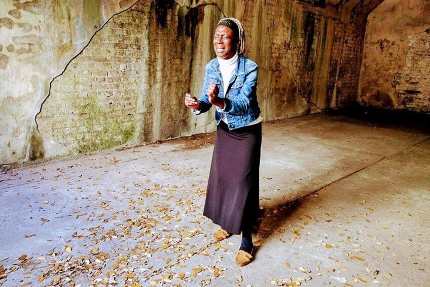A person in a denim jacket and skirt standing in an abandoned building with brick walls and scattered leaves on the floor. 3