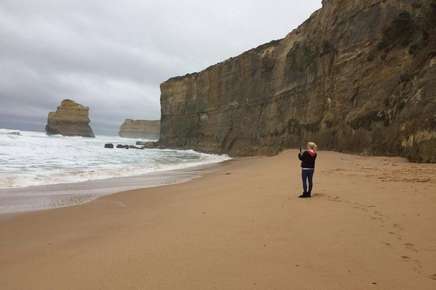 A person standing on a sandy beach with large rock formations in the background. 3