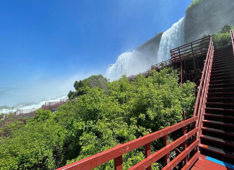 A waterfall cascading down a rocky cliff, surrounded by lush greenery and a wooden viewing platform. 2