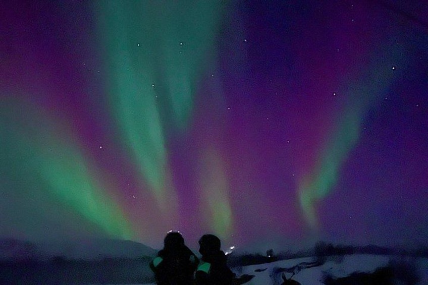 Norrsken över ett snötäckt landskap, där två personer står och betraktar det. 5