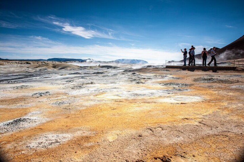 A geothermal area with steam vents and a group of people observing. 1