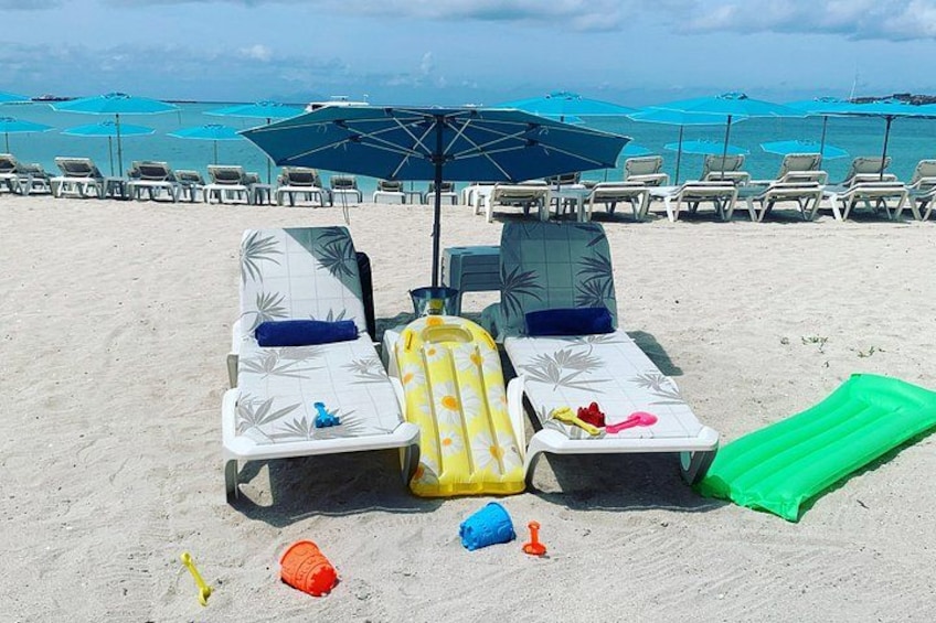 A beach with lounge chairs, umbrellas, and inflatable toys. 1