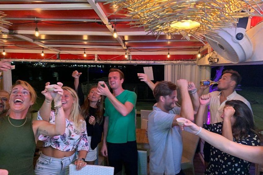 A group of people celebrating with drinks, a ceiling fan, and string lights. 4