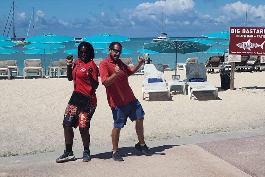 Two people posing on a beach with lounge chairs and umbrellas in the background. 2