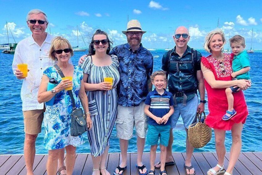 A group of people on a wooden dock by the sea with boats in the background. 2