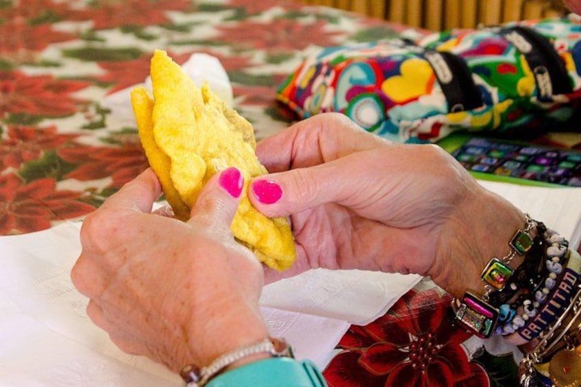 Hands holding a yellow object, possibly food, with colorful bracelets and a patterned fabric in the background. 4