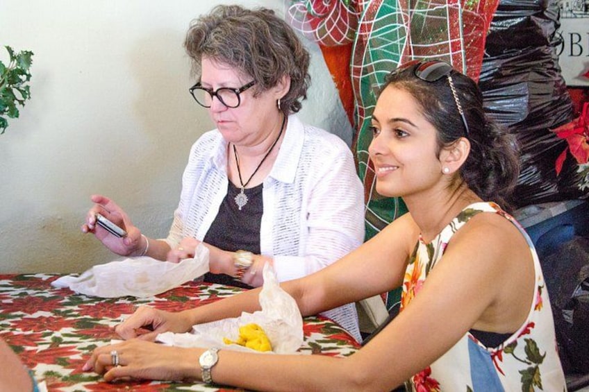 Two people sitting at a table with a patterned tablecloth, one holding a smartphone and the other with a yellow object. 2