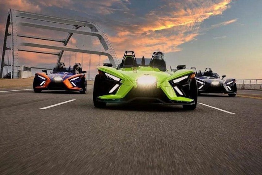 Three futuristic sports cars on a highway with a bridge in the background. 2
