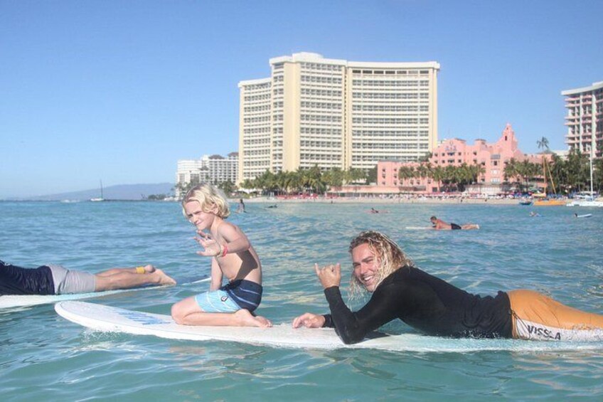 Two people on surfboards in the ocean with a resort and beach in the background. 2
