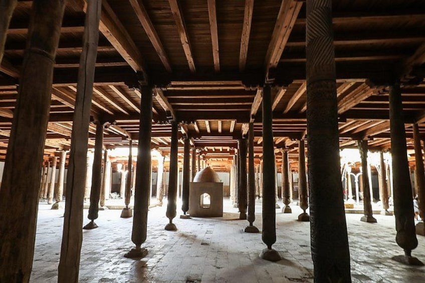 An interior with wooden beams and columns, a central arched doorway, and a patterned floor. 4
