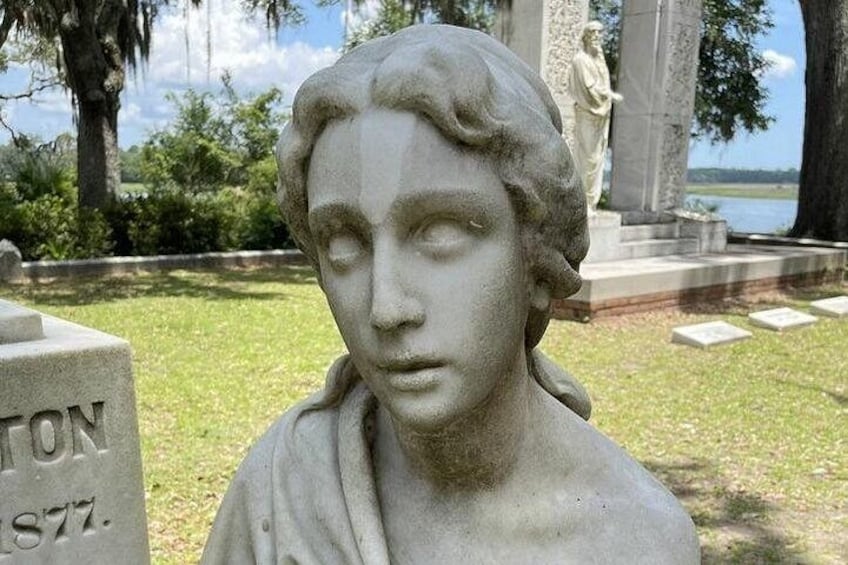 Ein Grabstein mit dem Namen 'TON 1877' und eine Statue im Hintergrund. 2