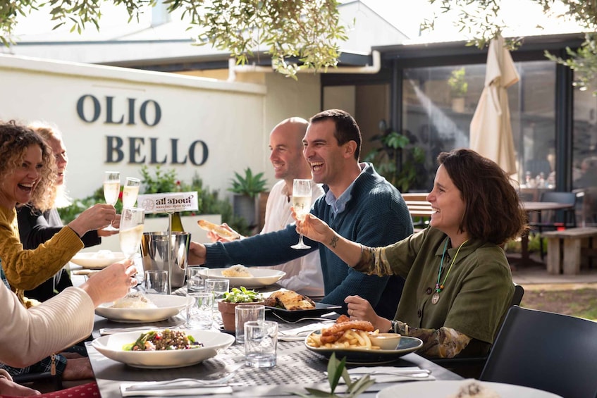 Eine Gruppe von Menschen speist draußen in einem Restaurant namens 'OLIO BELLO'. 1