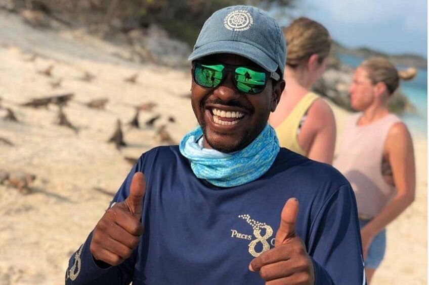 En person som visar tecknet ”tummen upp” på en sandstrand, med fåglar i bakgrunden. 5