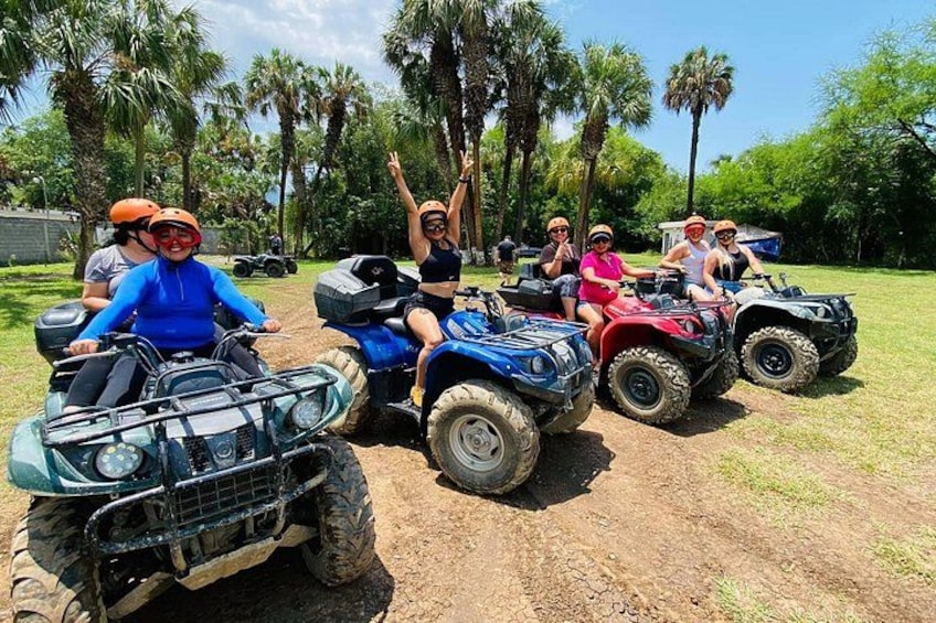 A group of people on ATVs in a grassy area with palm trees in the background. 1