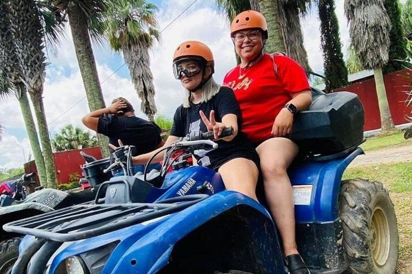 Two people on a blue Yamaha ATV, wearing helmets, with palm trees in the background. 2