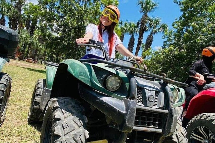 A person riding a green ATV in a grassy area with palm trees in the background. 3