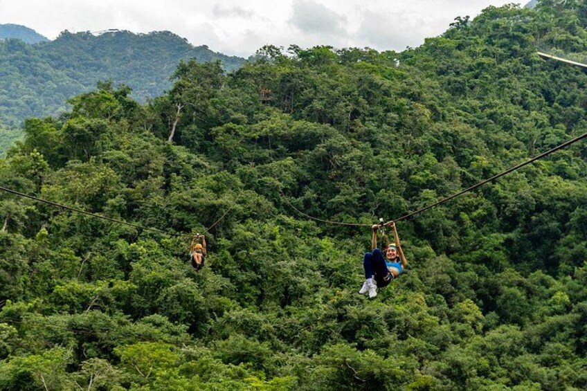 Twee personen zweven aan een kabelbaan boven een dicht bos. 2
