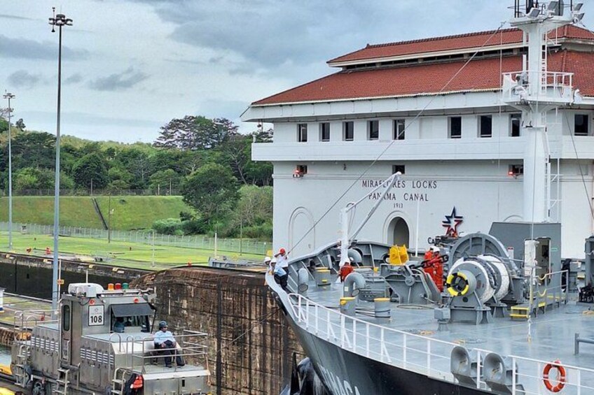 Ein großes Schiff liegt in einer Schleuse vor Anker, im Hintergrund ist ein Gebäude mit der Aufschrift 'Miraflores Locks Panama Canal' zu sehen. 4