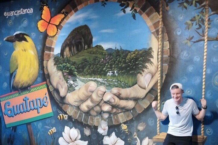 A man on a swing with a mural of a landscape and a bird. 5