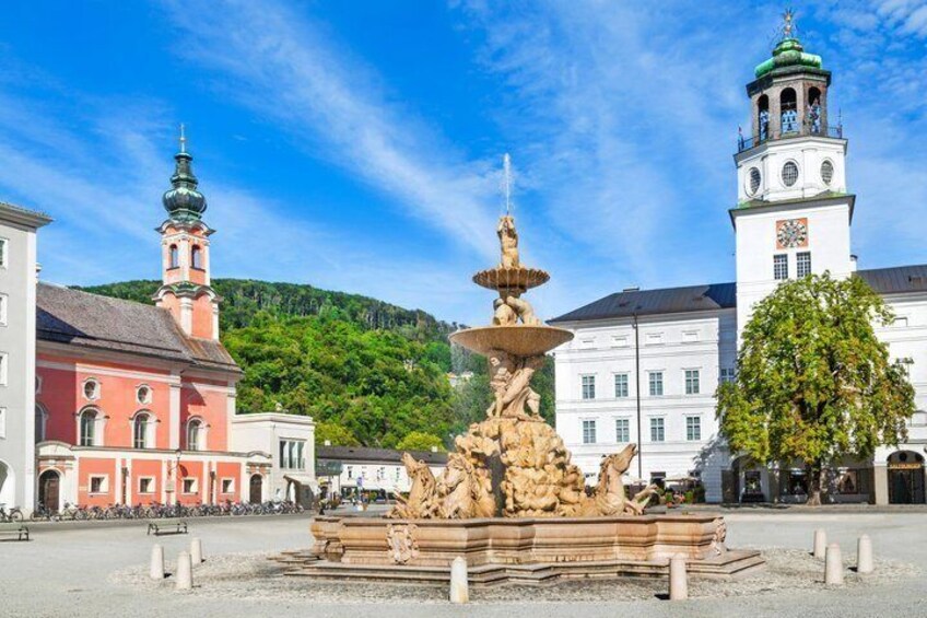 A historic fountain with multiple tiers and sculptures, surrounded by classical architecture and a hill in the background. 4